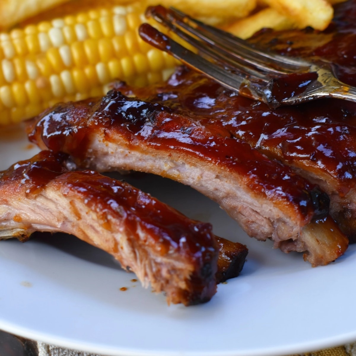 Zarte Schweinerippchen glänzen mit Bourbon-BBQ-Glasur neben knusprigen Süßkartoffel-Pommes, ein herzhaftes amerikanisches Gericht.