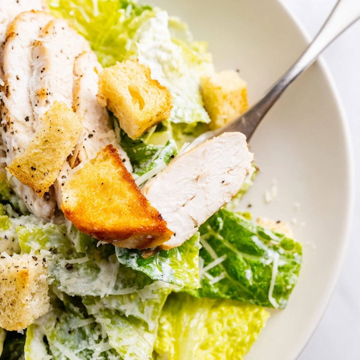 Freshly prepared Chicken Caesar Salad with Homemade Garlic Croutons, garnished with grated Parmesan and served alongside a glass of white wine.