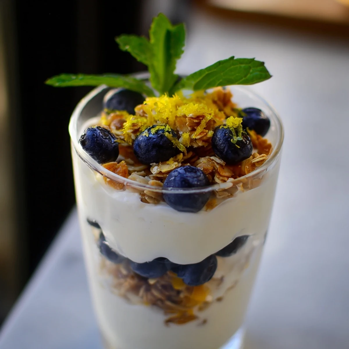 Frühstücksparfait aus Glas mit Schichten griechischem Joghurt, blauen Heidelbeeren und knusprigem Granola.