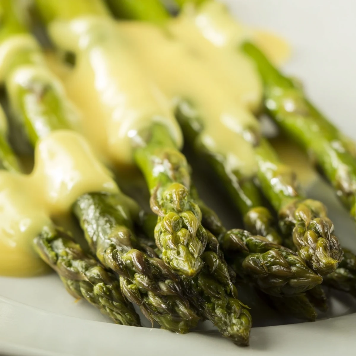 Roeasparagus with Hollandaise Sauce on a platter, smothered in velvety sauce and garnished with fresh chives.