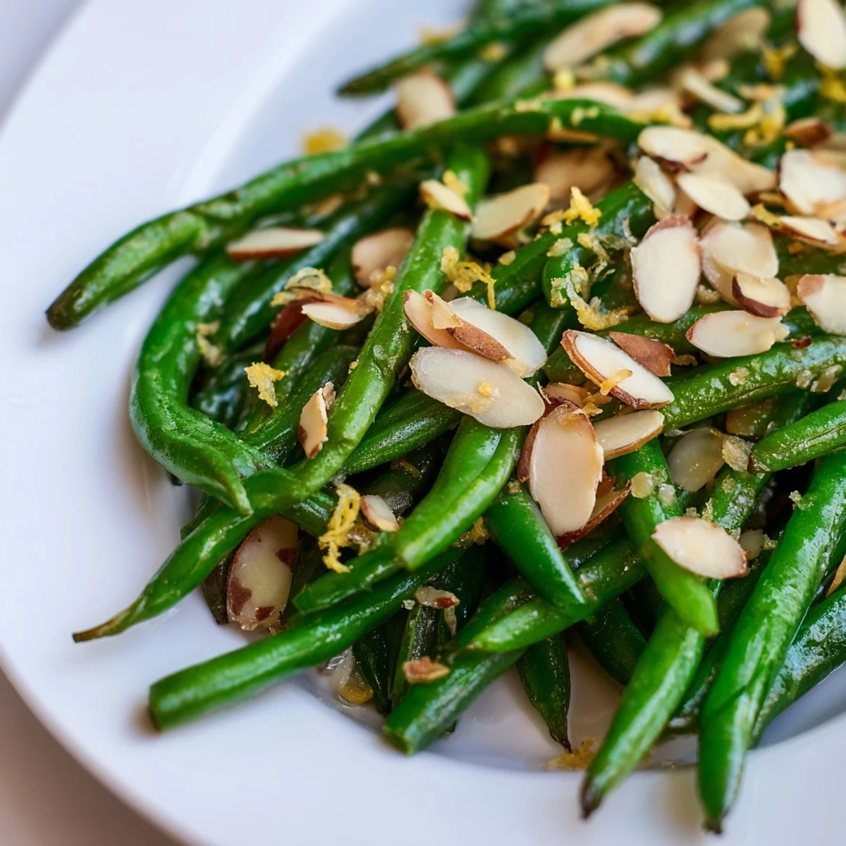 Bright green beans in Lemon Garlic Green Beans with Almonds topped with toasted almonds and fresh lemon zest on a white plate.