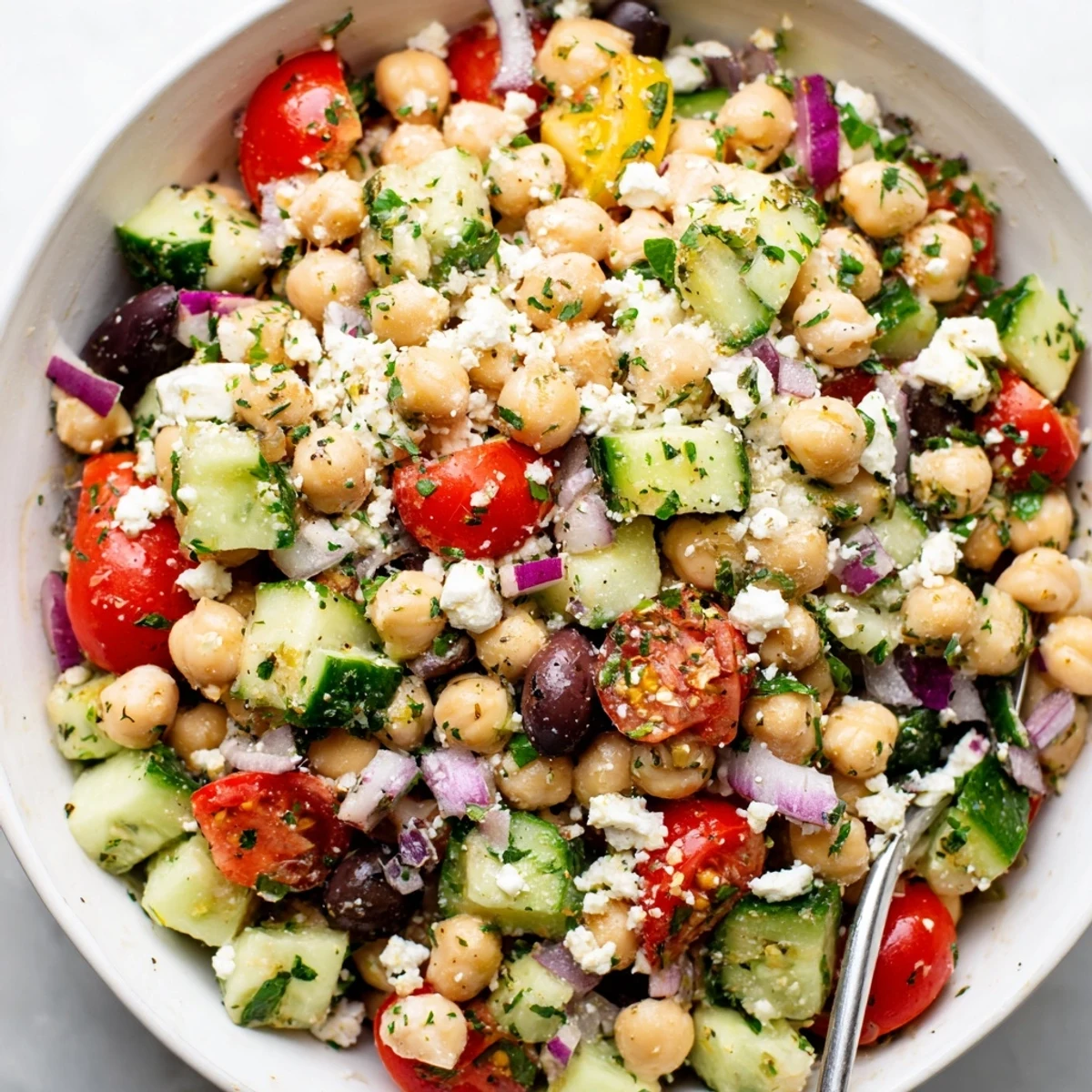 A vibrant Mediterranean Chickpea Salad with Feta, featuring crisp cucumbers, juicy tomatoes, and Kalamata olives, served in a white bowl.