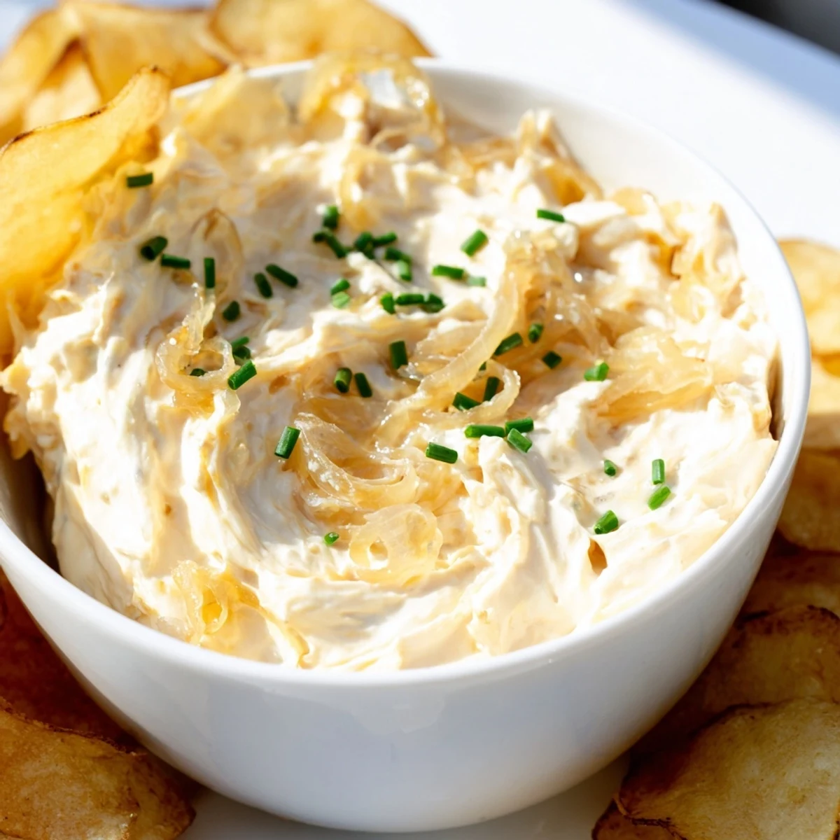 A bowl of creamy onion dip with crispy potato chips, garnished with fresh chives, ready for snacking or parties.