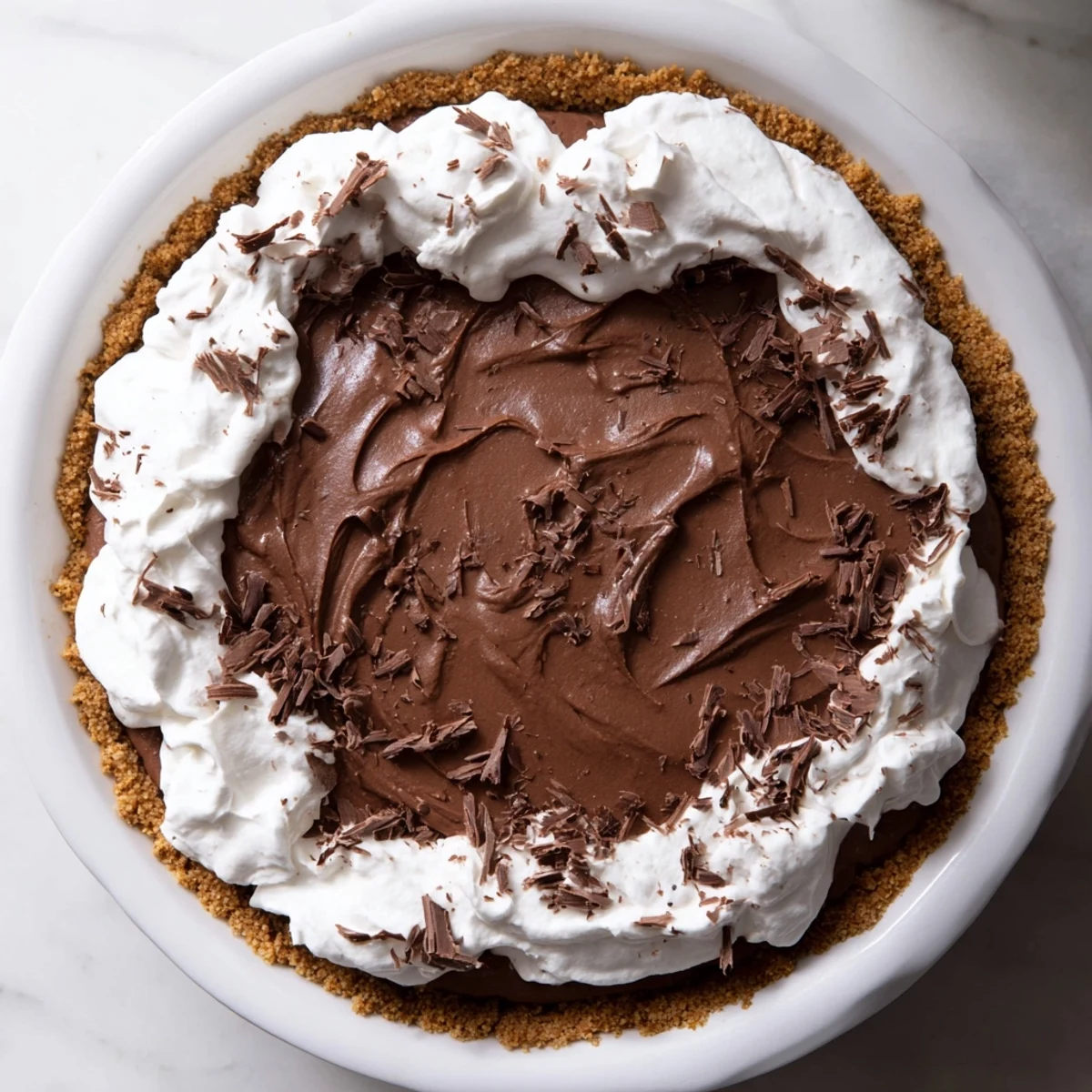 Ein frisch aufgeschlagener Haufen Schlagsahne auf einem reichhaltigen Schokoladenkuchen, auf dessen Oberfläche sich zarte Schokoladenspäne befinden.