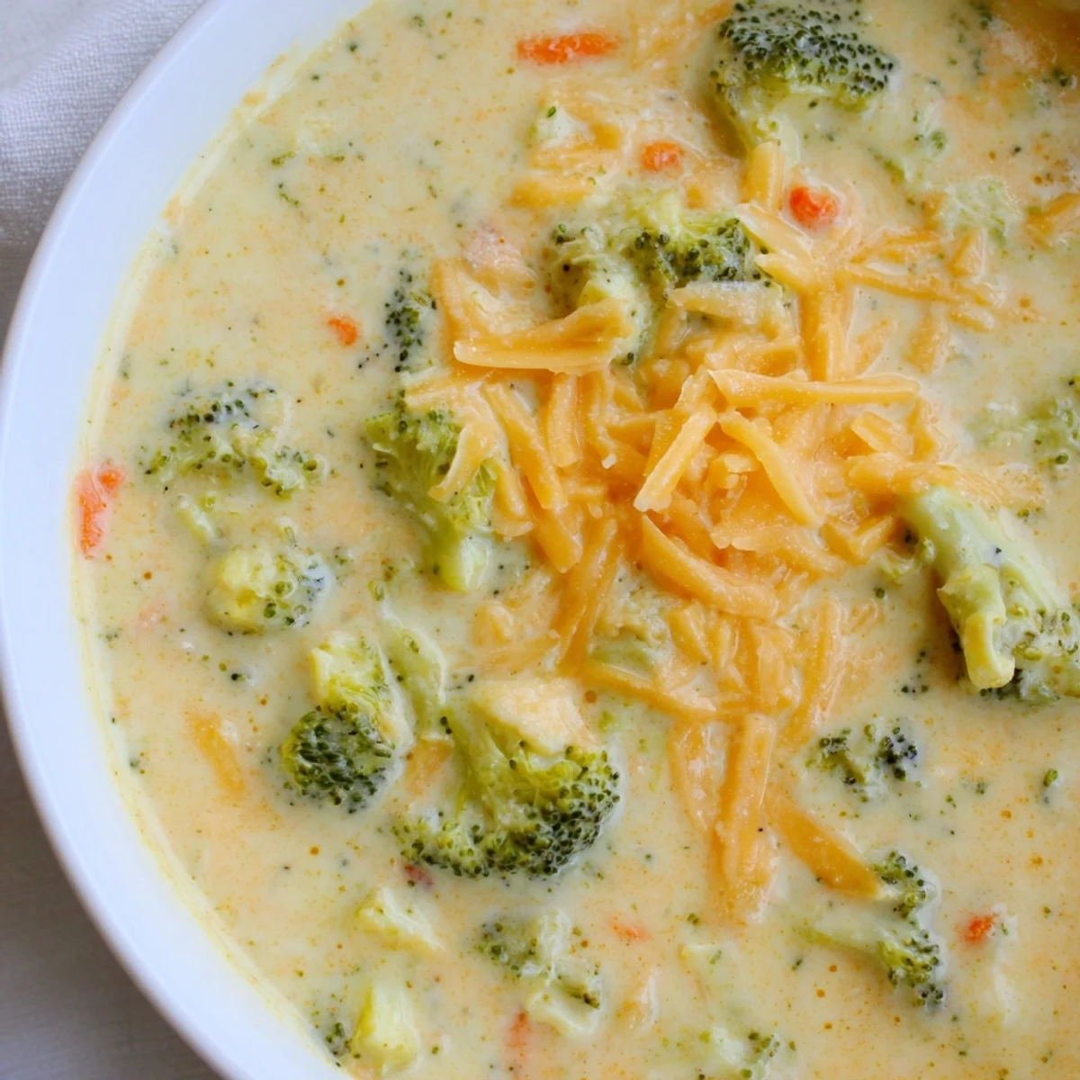 Velvety creamy broccoli cheddar soup garnished with extra cheese and fresh herbs, ideal for cozy lunches.
