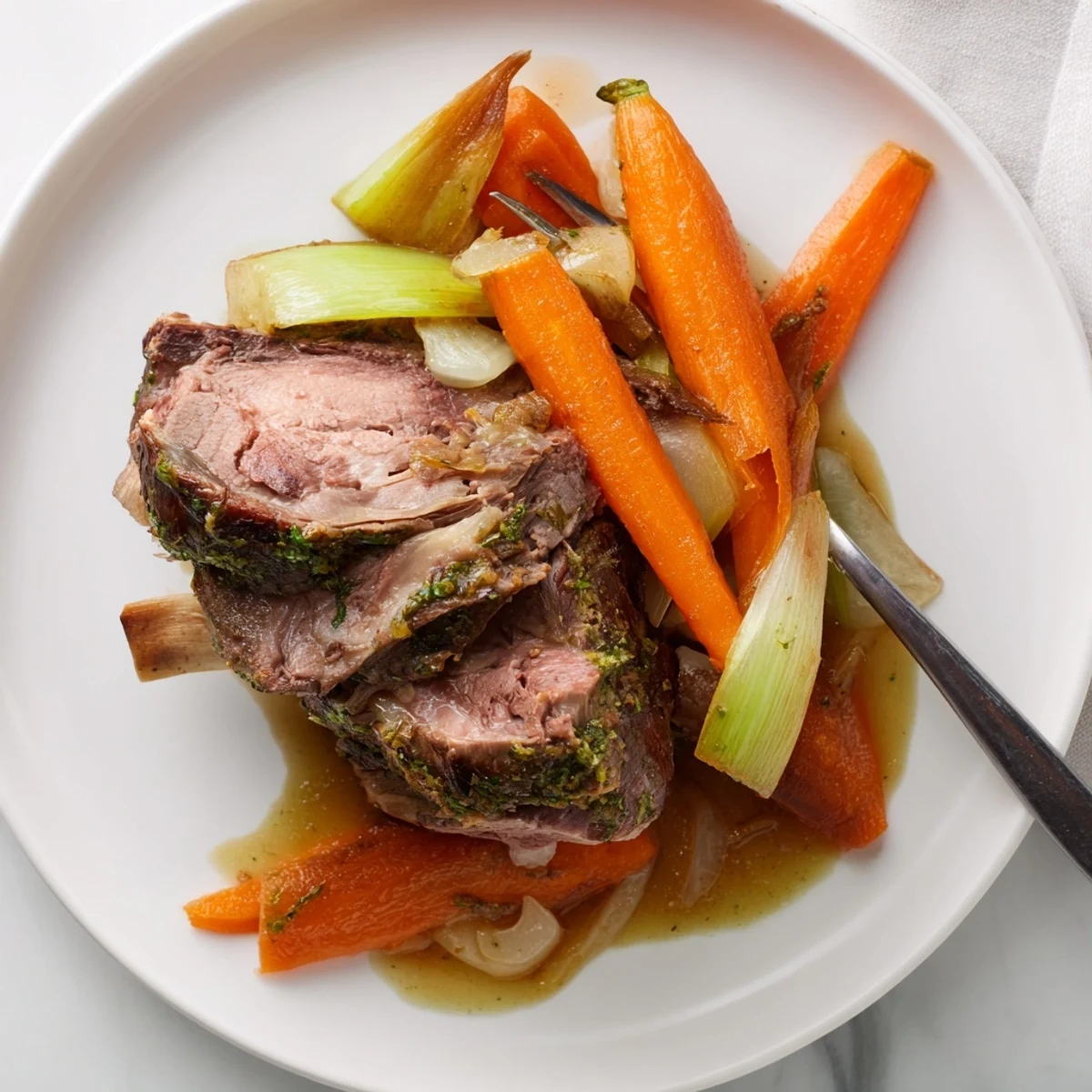 Genussreifes Lamm-Schulterstück mit frischen Kräutern und einem glänzigen Sud, serviert mit Gemüse.