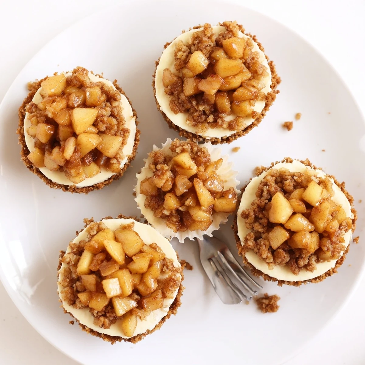 Creamy mini cheesecakes topped with warm spiced apple crisp crumble on white plate