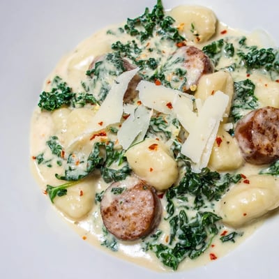 Creamy Gnocchi with Sausage and Kale served on a white plate next to a glass of red wine