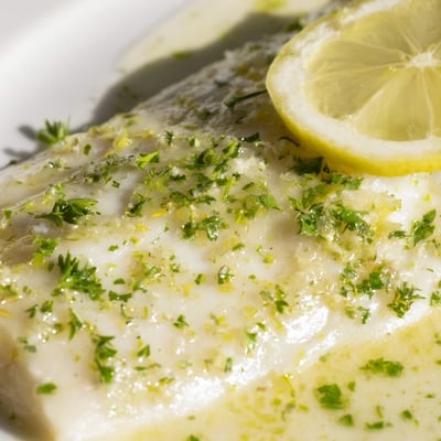 Zarter, saftiger Halibut mit duftender Zitronenbutter-Sauce und frischer Petersilie auf einem blauen Teller.