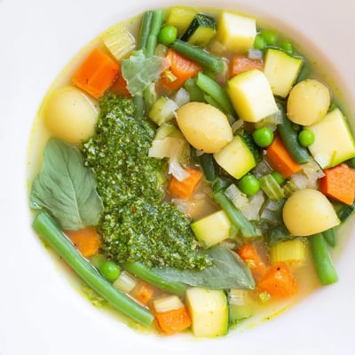Spring Vegetable Soup with Pesto Swirl in einer Schüssel mit goldenem Ölstrudel.